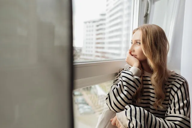 A woman in her late thirties looking thoughtfully at a sunlit window