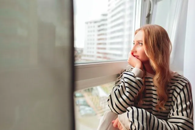 A woman in her late thirties looking thoughtfully at a sunlit window